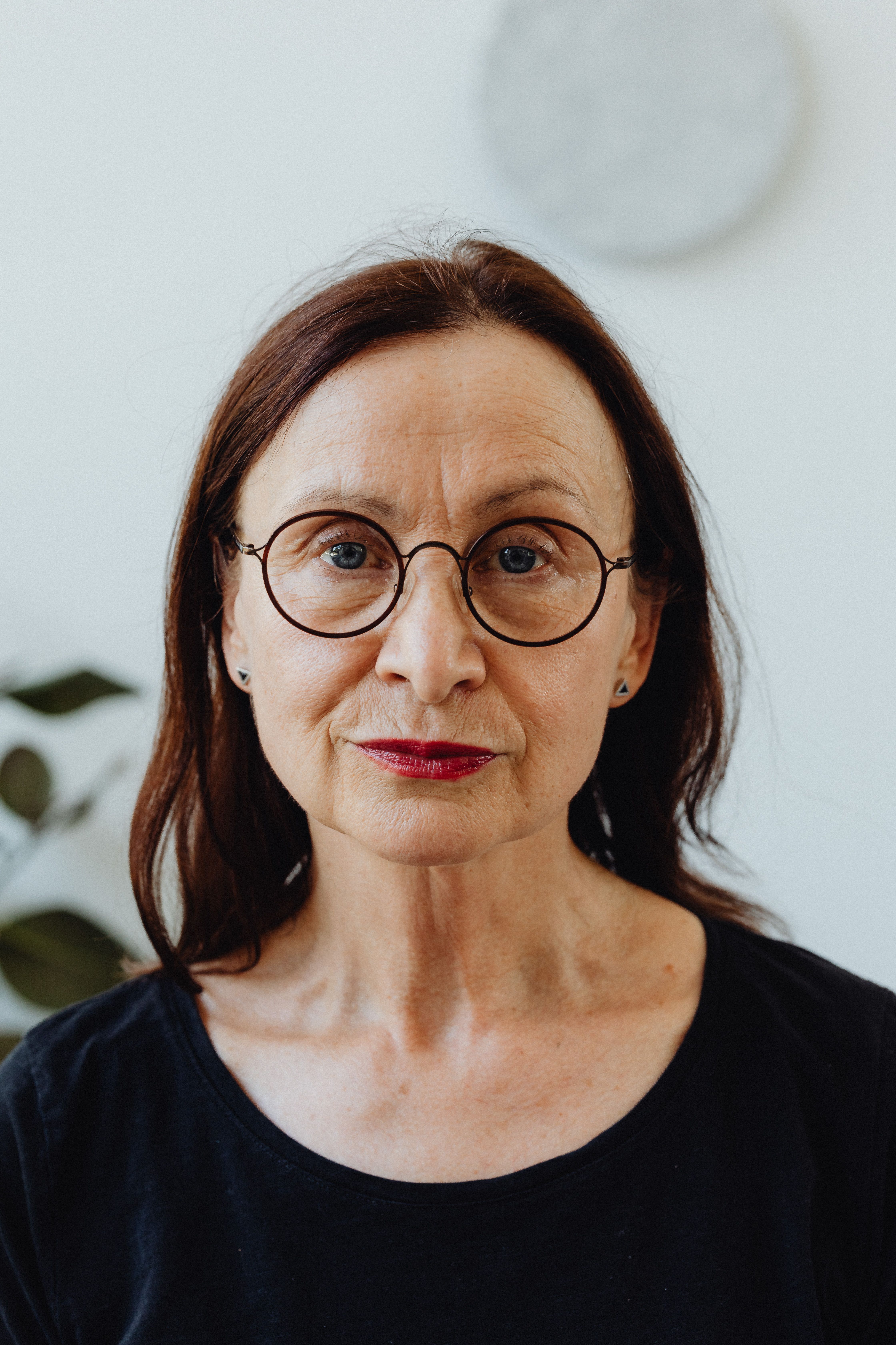 Close-up portrait of an elderly woman with eyeglasses and a neutral expression indoors.