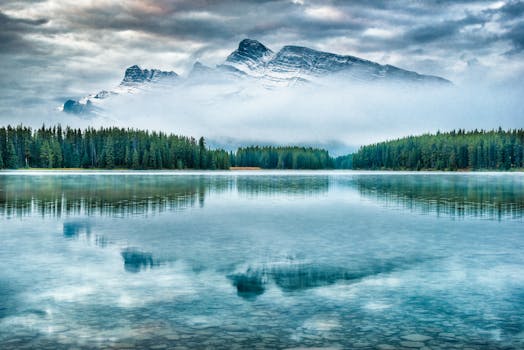 Stunning view of mountain reflection in Alberta's calm lake, surrounded by lush pine forest.