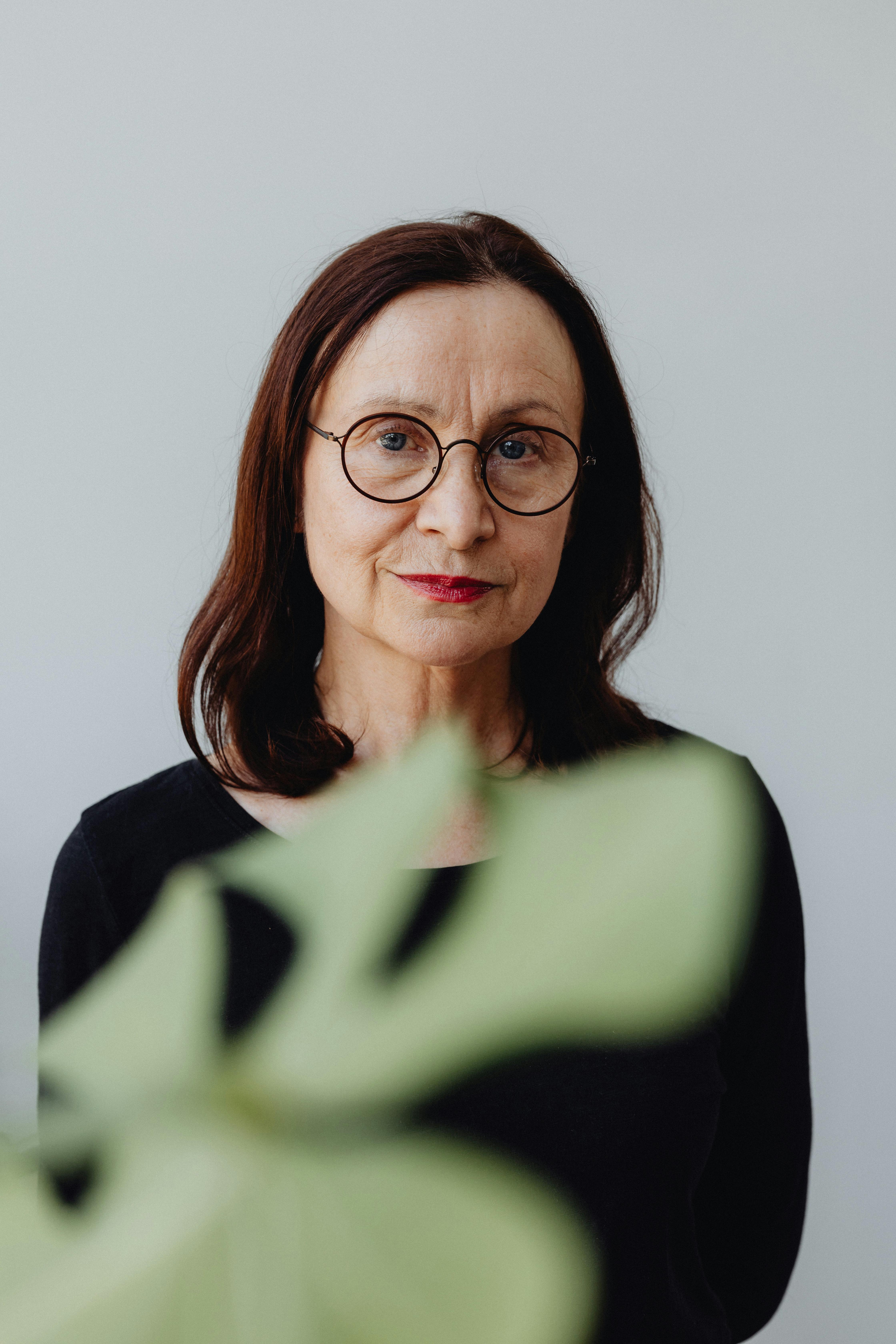 Charming portrait of a senior woman with eyeglasses and a captivating smile, set against a soft background.