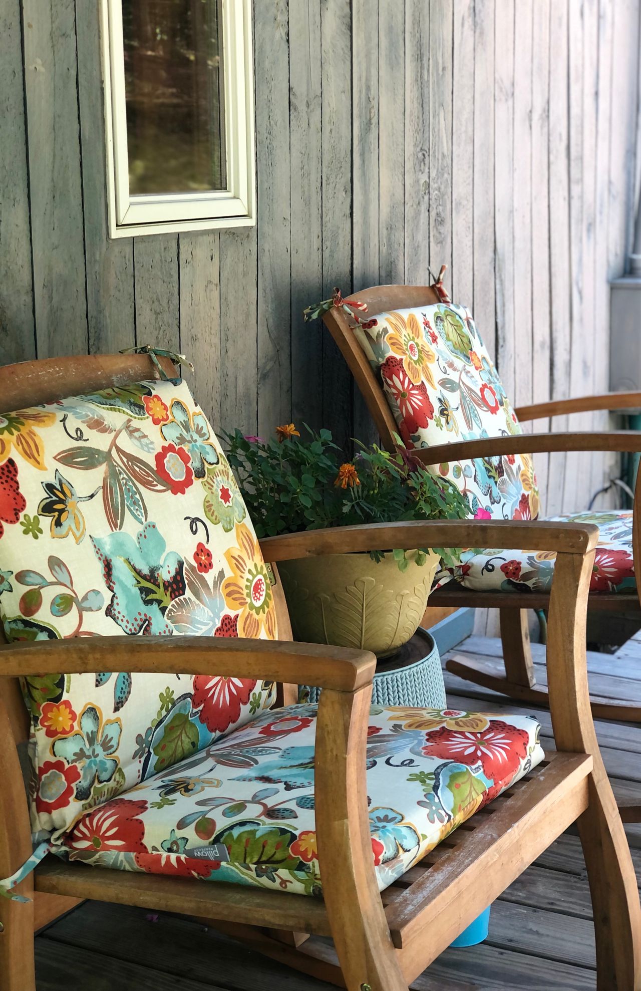 Wooden porch chairs with floral cushions against weathered gray shingle siding