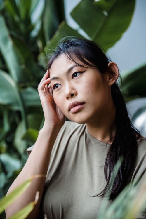 Free Close-up portrait of a young woman surrounded by lush green plants, conveying a contemplative mood. Stock Photo
