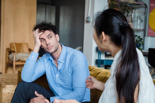 Free A tired man in a blue shirt listens while a woman talks indoors. Modern living room. Stock Photo