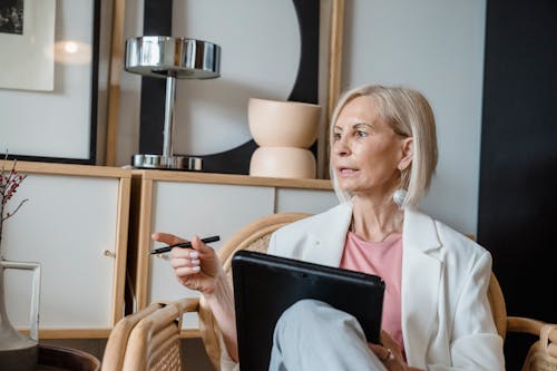 Woman in White Blazer Holding Pen While Sitting on Chair 