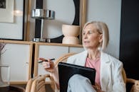 Woman in White Blazer Holding Pen While Sitting on Chair