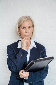 Confident businesswoman with tablet posing against a white brick wall.