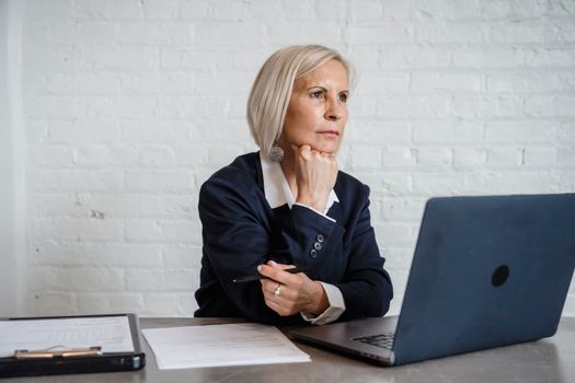 Professional woman in deep thought, working on a laptop indoors, suggesting mental focus and business acumen.