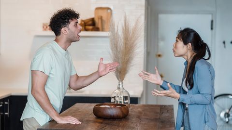 A couple engages in a heated argument at a wooden table in a modern indoor setting.