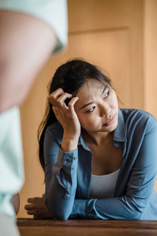 Free Thoughtful Asian woman in blue shirt indoors, appearing concerned and reflective. Stock Photo