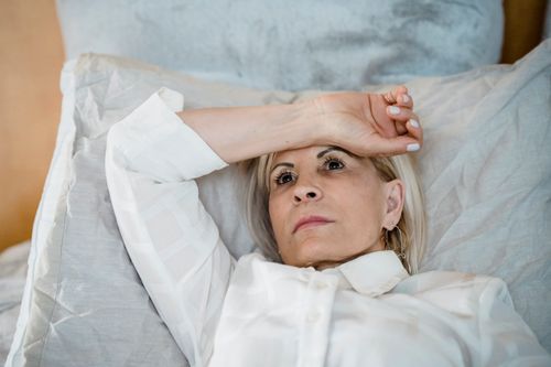 Free Contemplative woman in white shirt lying on bed, lost in thought. Indoor setting highlights tranquility. Stock Photo