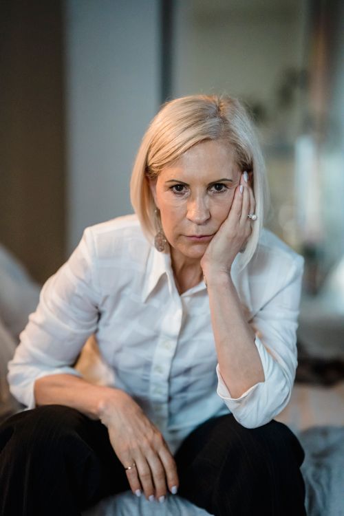 Free Thoughtful woman sitting with hand on cheek in an indoor setting. Stock Photo