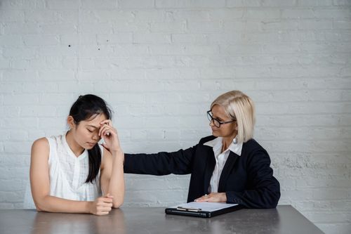 Free A supportive counseling session where one woman comforts another at a table against a brick wall. Stock Photo