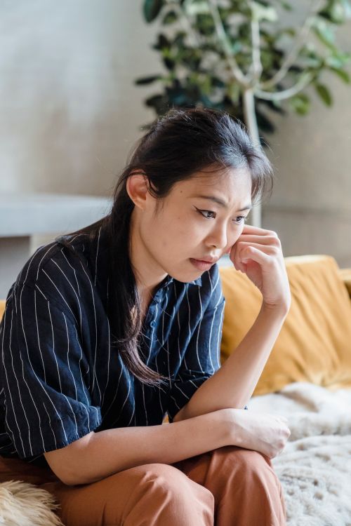 Free Thoughtful young woman sitting indoors, contemplating and reflecting. Stock Photo