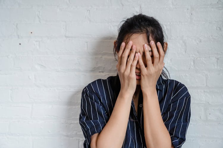 A Frustrated Woman Leaning On A White Wall While Covering Her Face