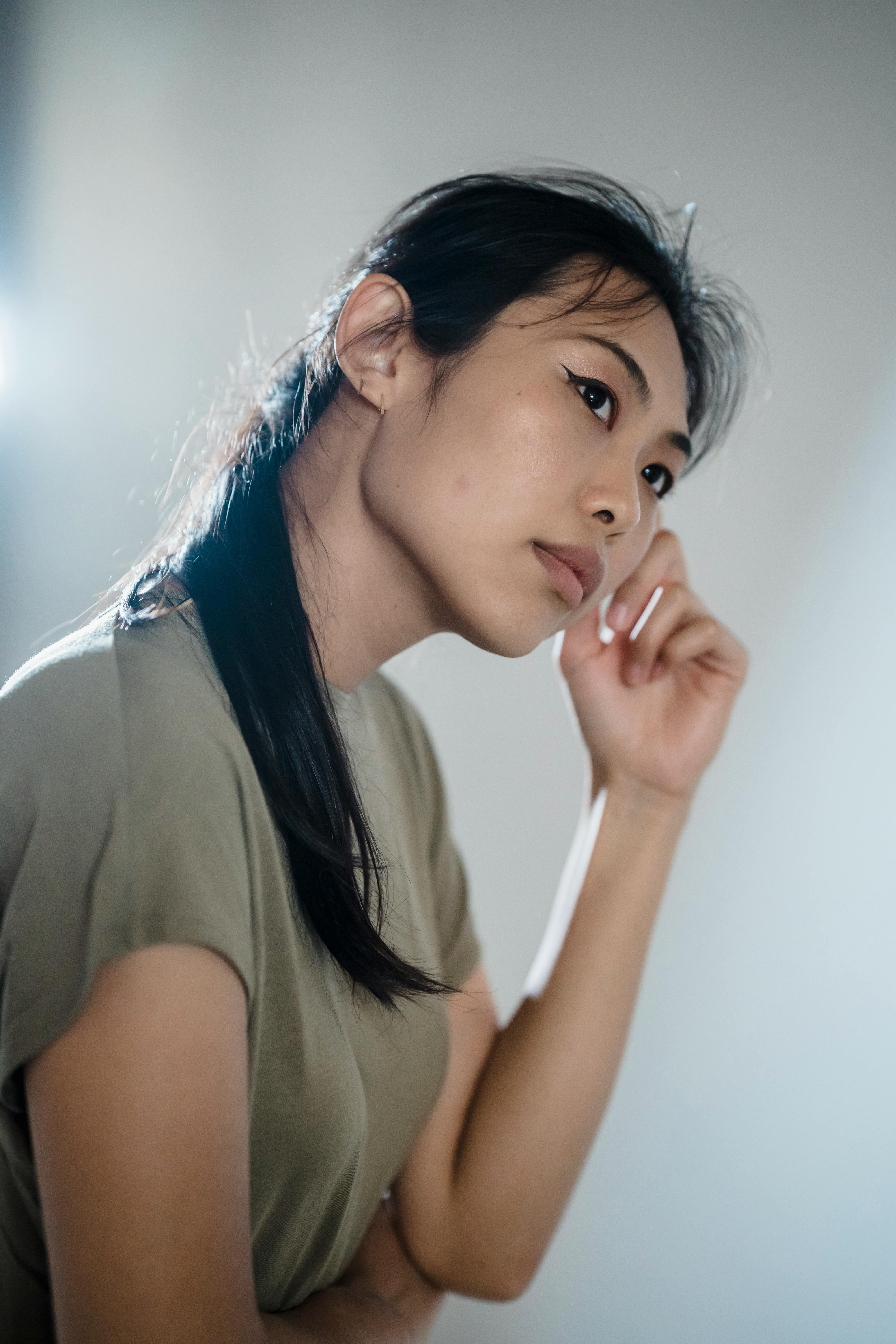 Captivating portrait of an Asian woman in deep thought, indoors in soft lighting.