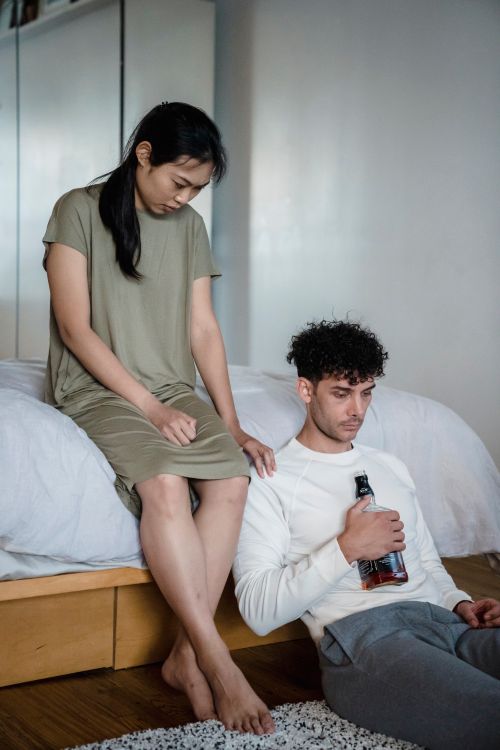 Free A concerned couple sitting in a bedroom, man holding a bottle. Emotional tension. Stock Photo