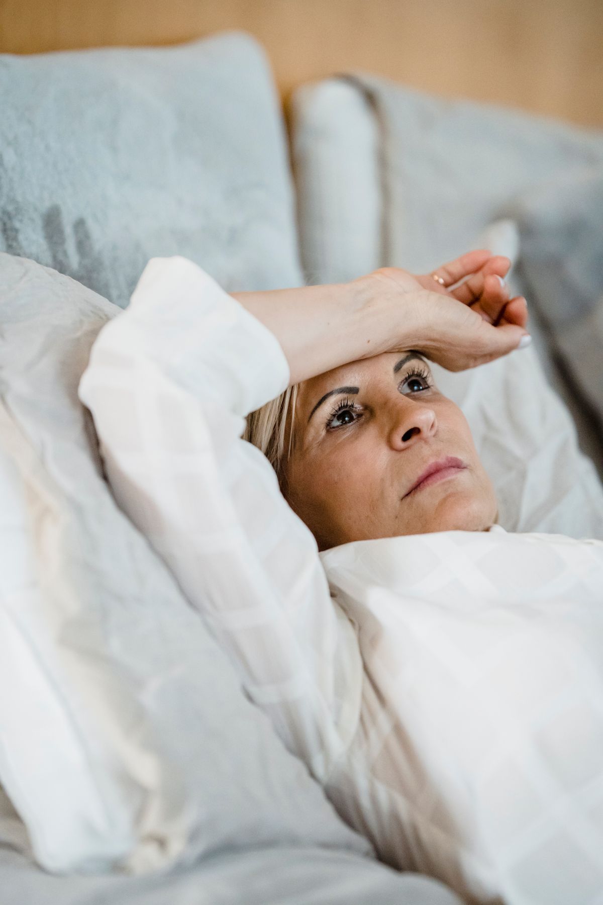 A woman in her mid-40s lying awake in bed at night, hand on her forehead, unable to sleep.