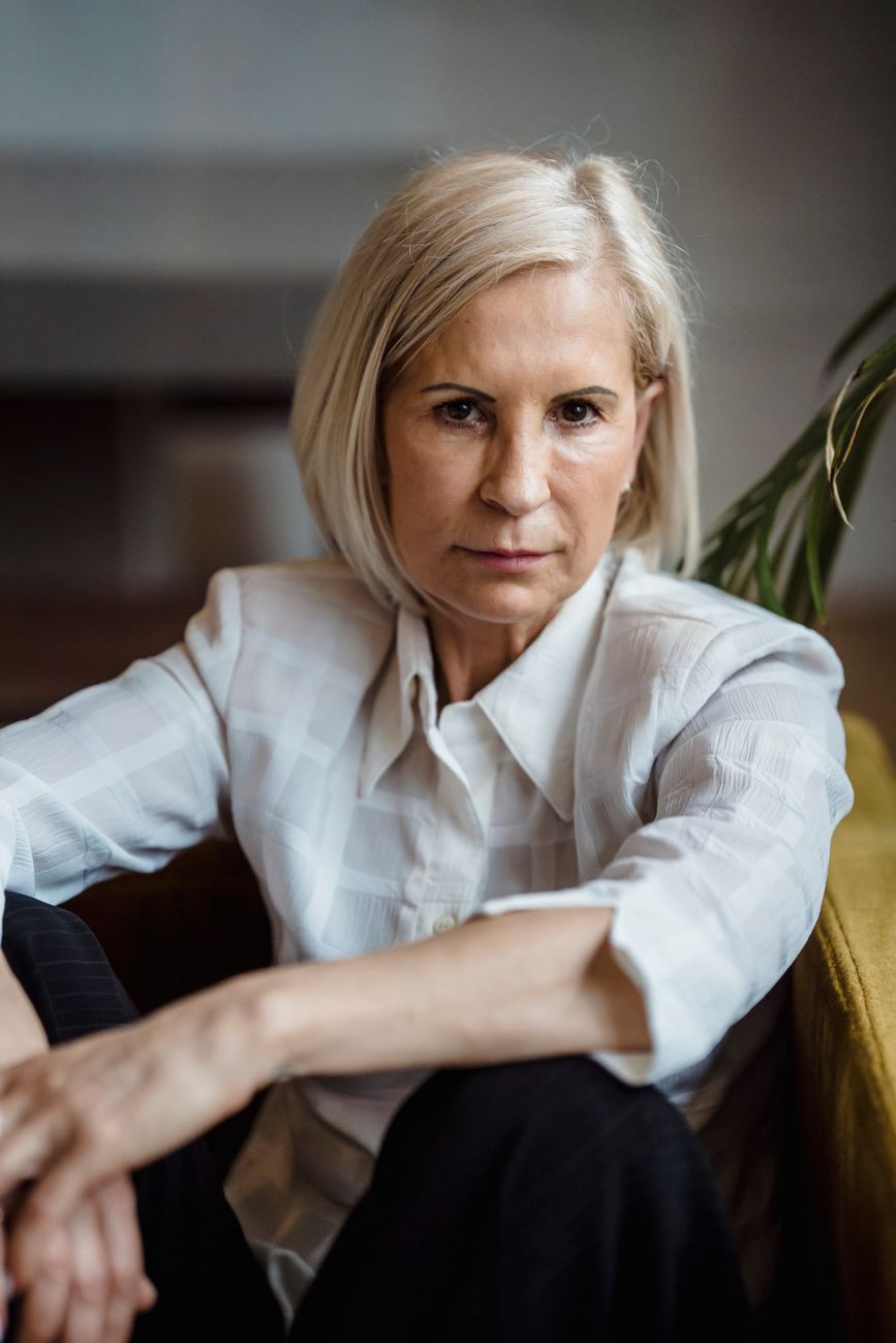 Elegant portrait of a pensive mature woman with blonde hair, sitting indoors. Captured in natural light.