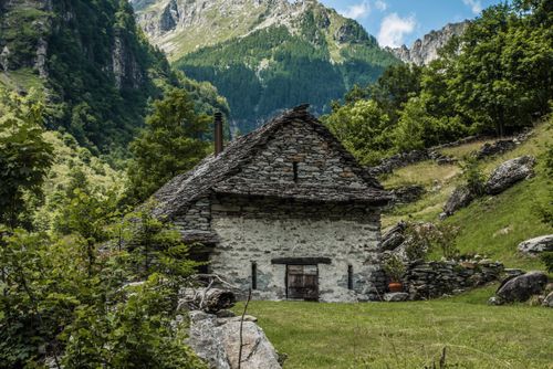 Free Charming stone cottage nestled in lush greenery and mountain landscape. Stock Photo
