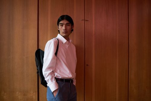 Free Portrait of a young man in white shirt and backpack standing against a wooden wall. Stock Photo