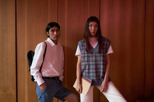 Fashionable students posing against a wooden wall, showcasing modern academic style.