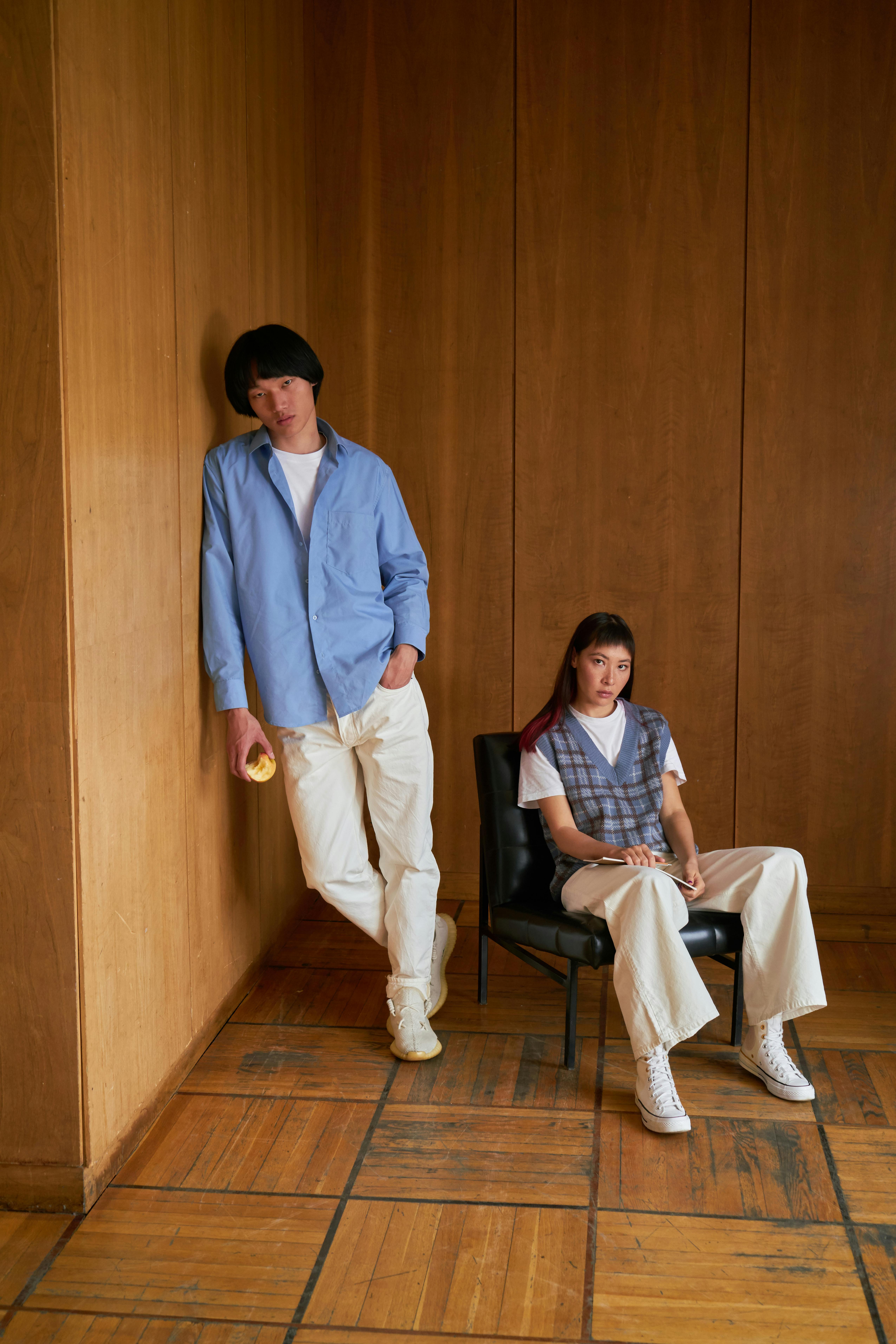 Free Two adults in casual attire pose against wooden wall indoors. Stock Photo