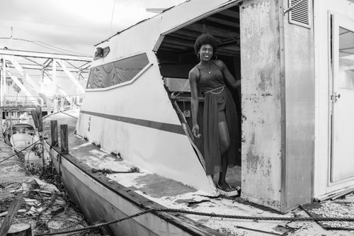 Free Black and white portrait of a woman posing on a weathered boat, exuding a gritty charm. Stock Photo