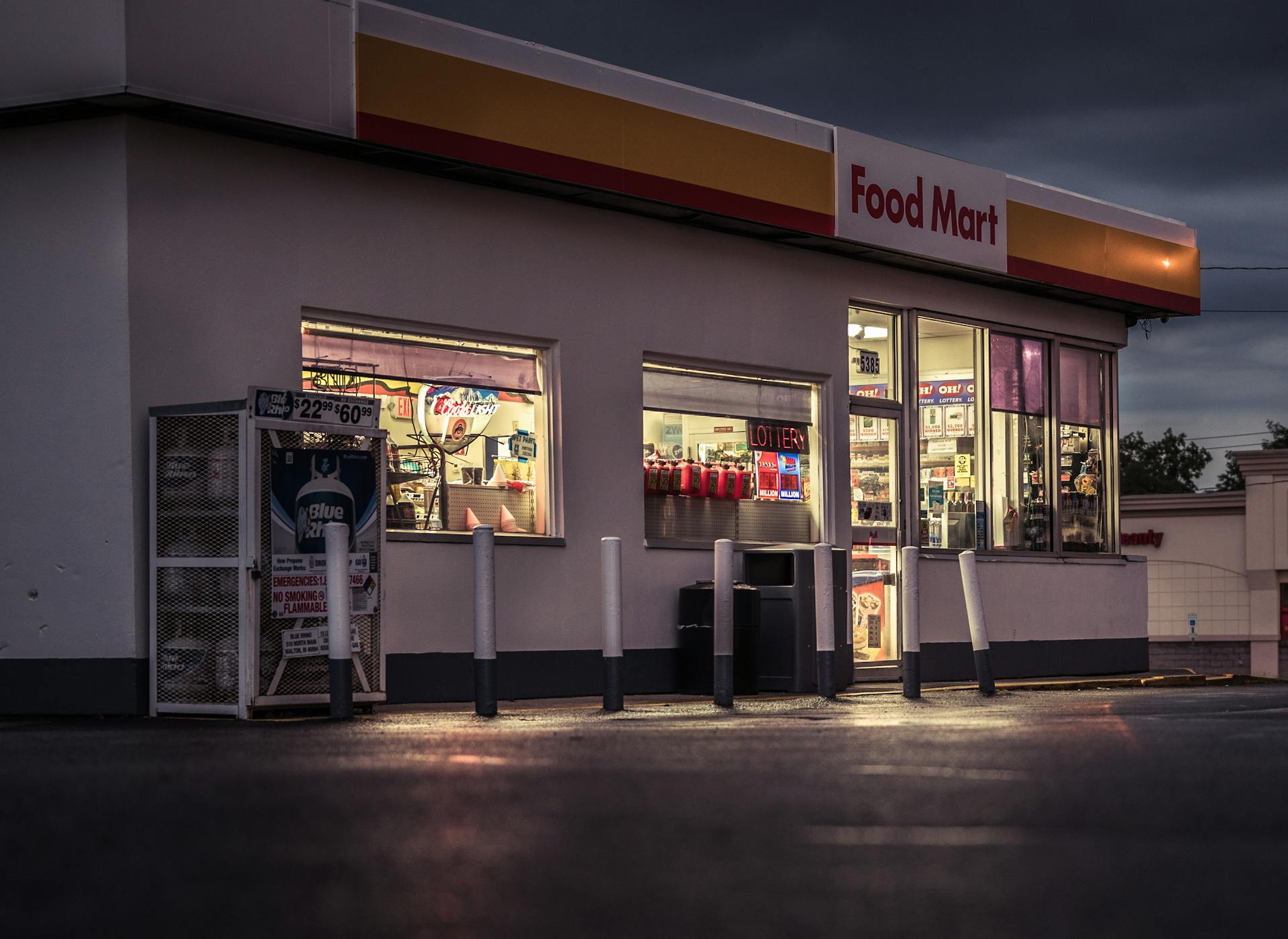 Exterior view of a food mart at night with illuminated signage and bollards.