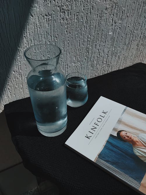 Clear Drinking Bottle and Glass and Kinfolk Magazine on Black Table