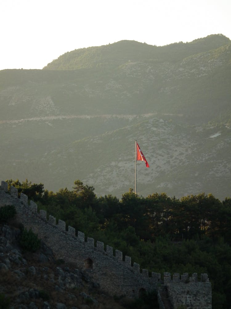 Red Flag On Pole Near Green Trees