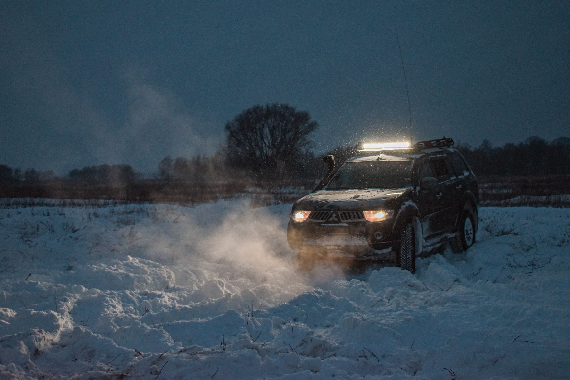 SUV pushing through deep snow in an open field at dusk