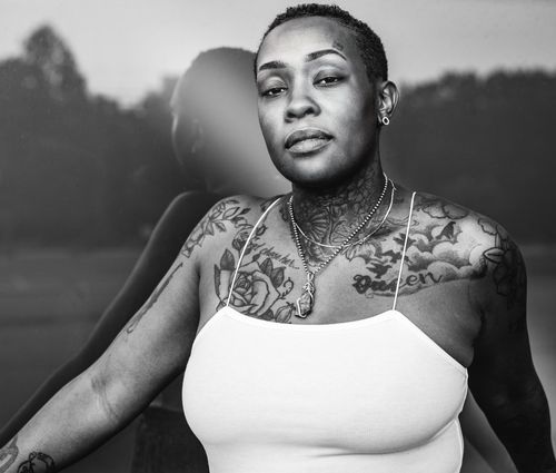 Free Grayscale portrait of a tattooed woman in a white tank top, exuding confidence. Stock Photo