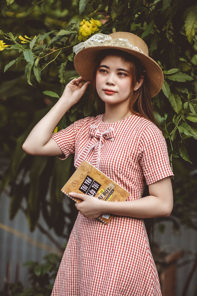 Young Woman In Red And White Plaid Dress Holding Brown Notebook