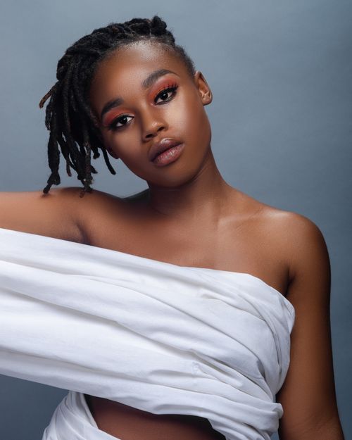 Free Studio portrait of a woman with dreadlocks, bare shoulders, and white fabric on a gray background. Stock Photo