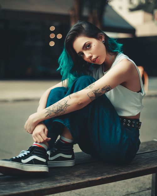 Free Stylish young woman with blue hair sitting on a bench, showcasing tattoos and fashion. Stock Photo