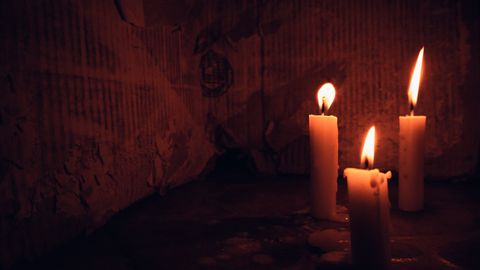 Three candles burn with a warm glow, creating a cozy ambiance in a dimly lit room.