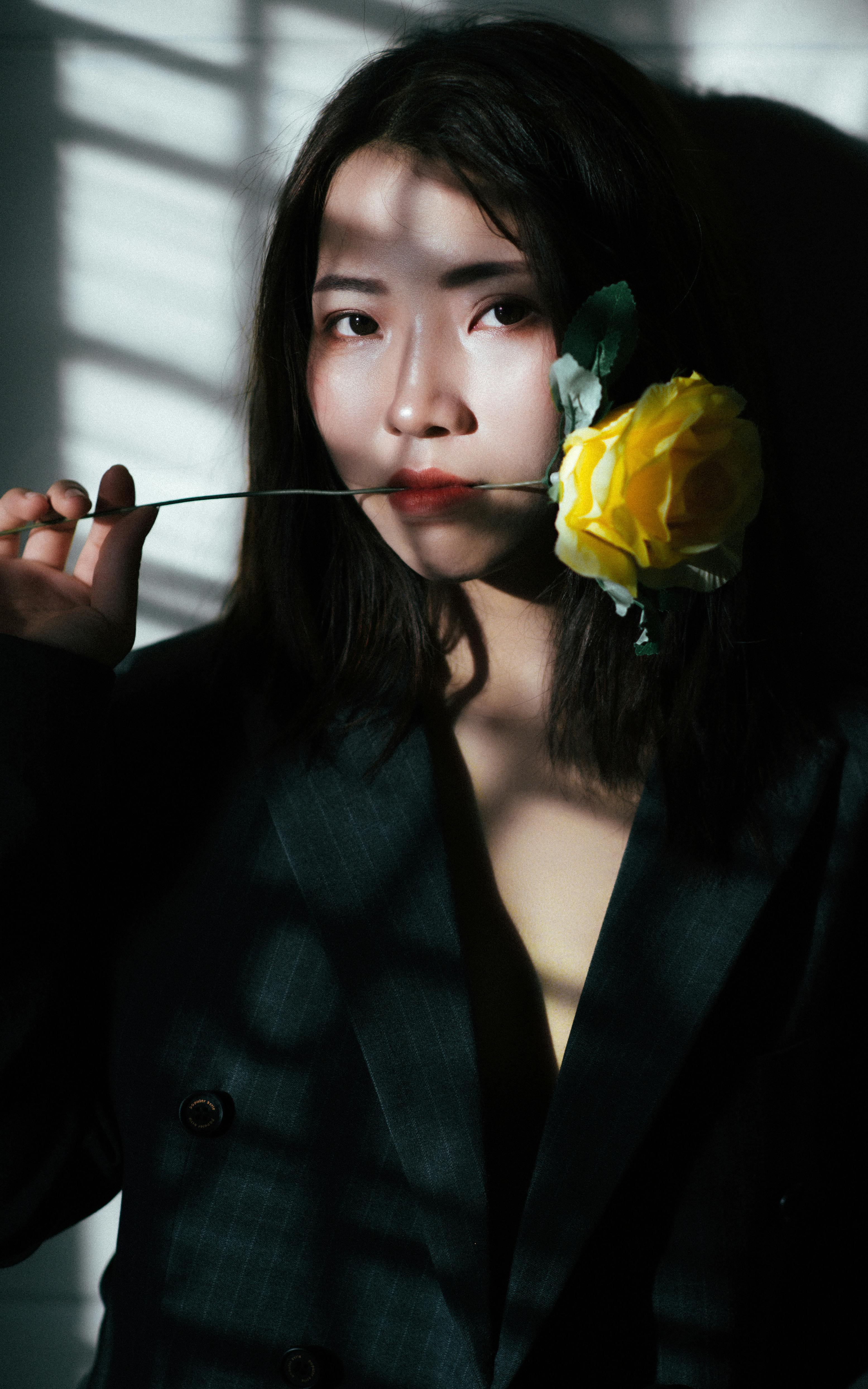 Elegant portrait of a woman holding a yellow rose, with striking light and shadow contrasts.