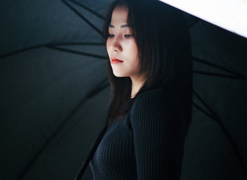 Close-up of a woman in a black sweater holding a black umbrella, looking down.
