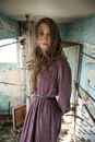 Gentle young slender female in trendy dress looking at camera in weathered building with blue old walls