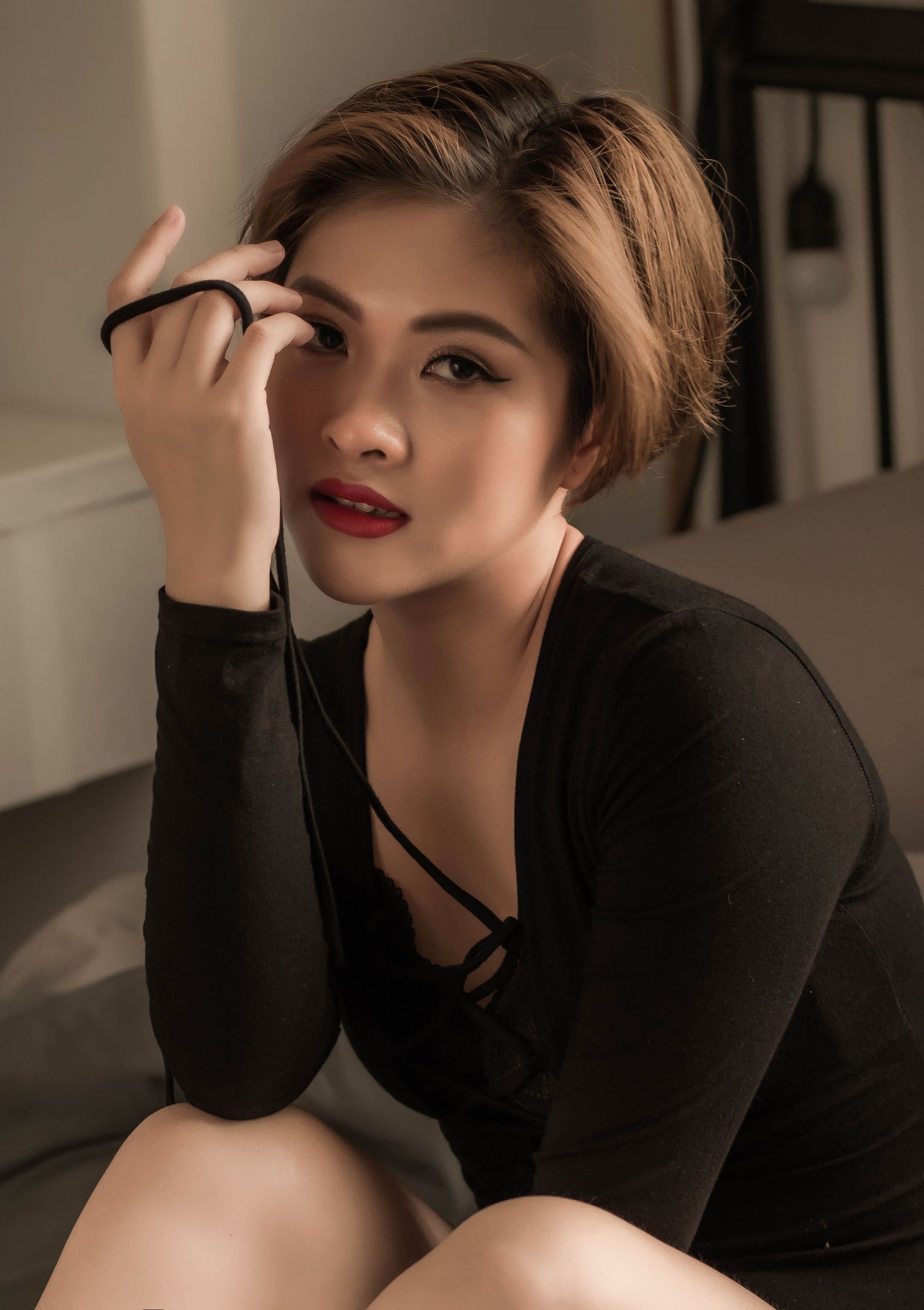 Elegant portrait of an Asian woman showcasing modern fashion with short hair and dark attire, posed indoors.