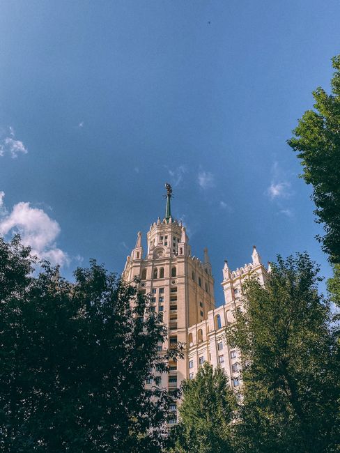 Low angle view of Stalinesque skyscraper in Moscow with a clear blue sky and trees.