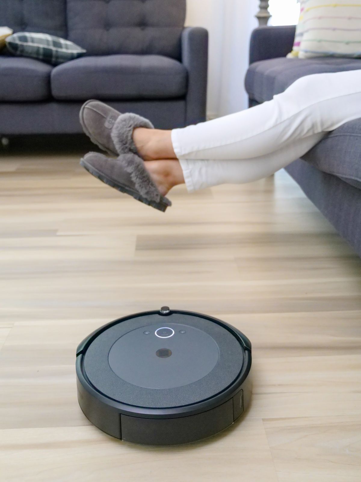 A black robot vacuum cleaning a hardwood floor in a spacious living room