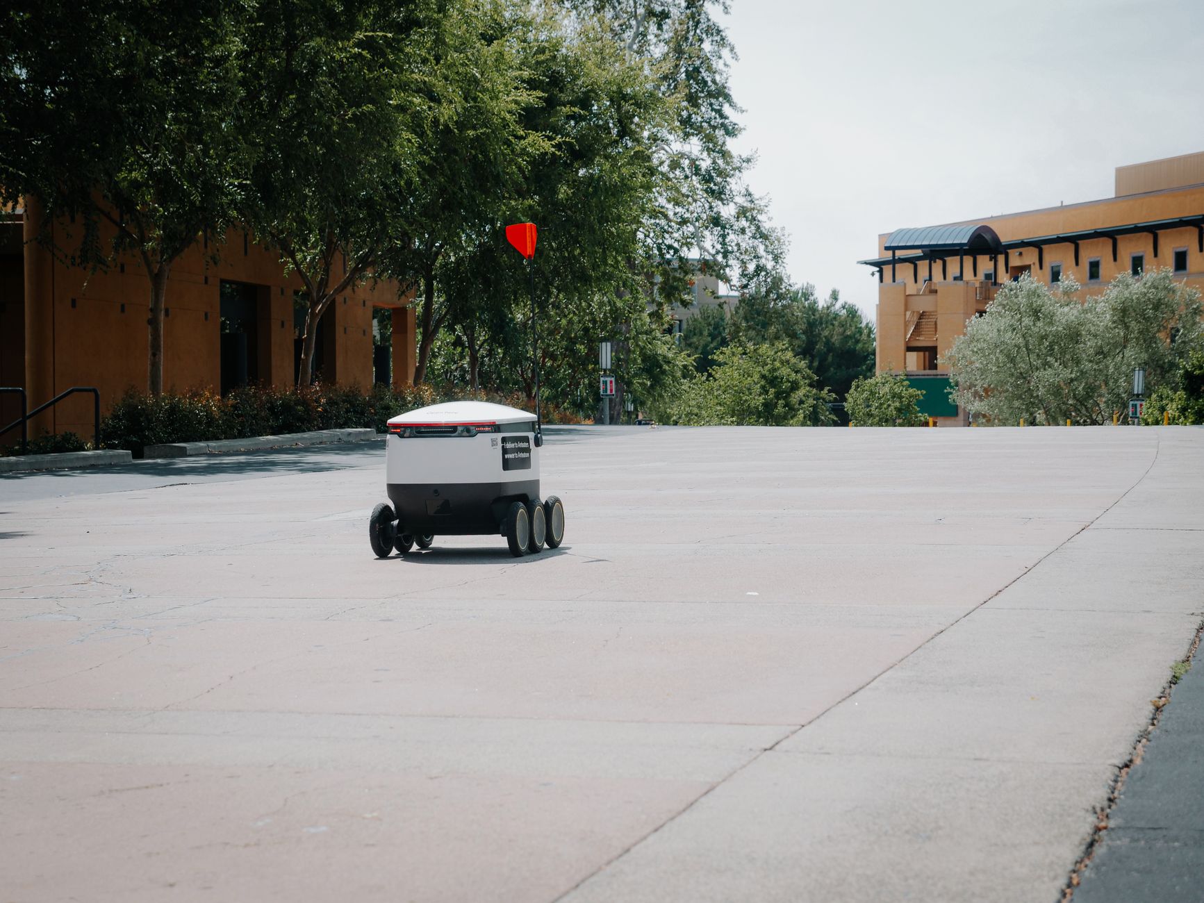 A futuristic autonomous delivery robot moving on an empty city street.
