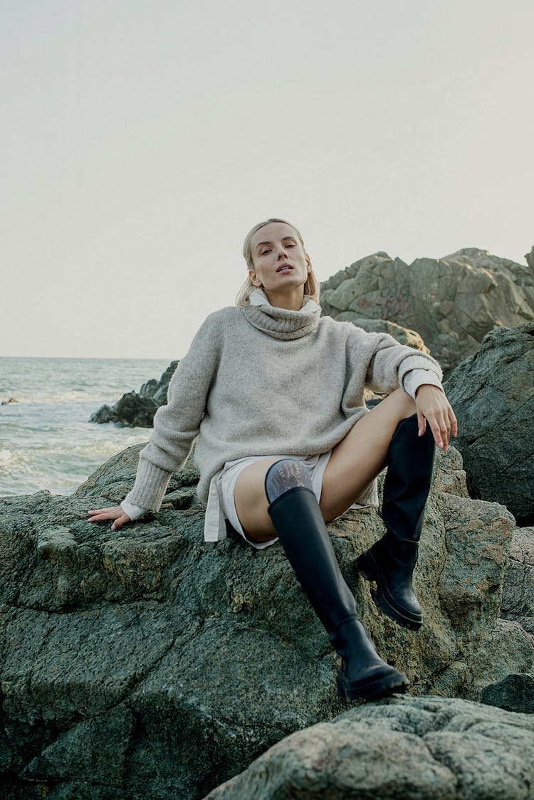 Woman Sitting On A Large Rock On A Seashore 