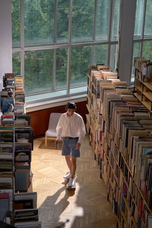 Free A young man on a skateboard explores the library aisle next to sunlit bookshelves. Stock Photo