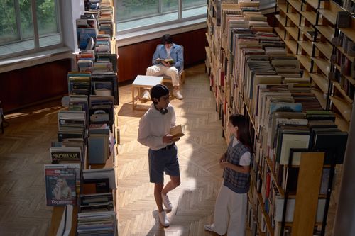 Free Three students in a library reading and discussing books under natural light. Stock Photo