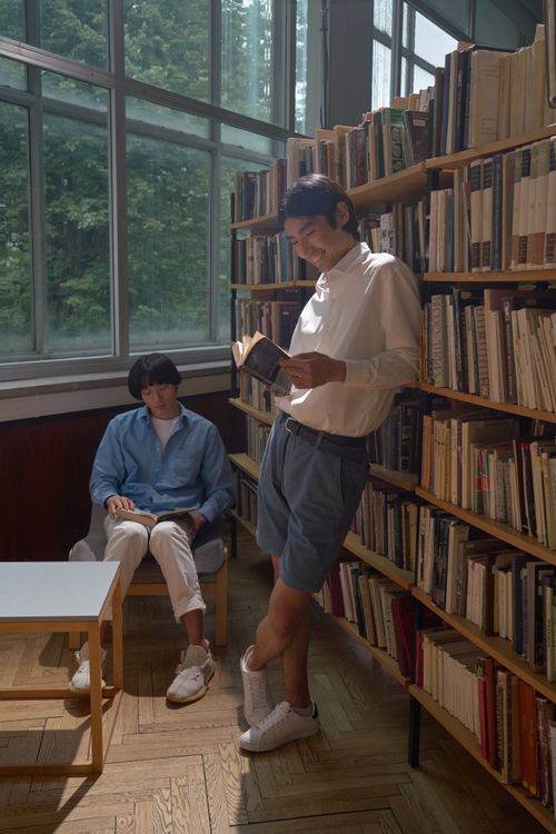 Free Two people reading in a cozy library setting filled with books and natural light. Stock Photo