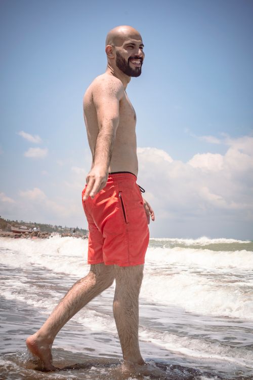 Free Bald man in red shorts, smiling at İskenderun beach on a sunny day. Stock Photo