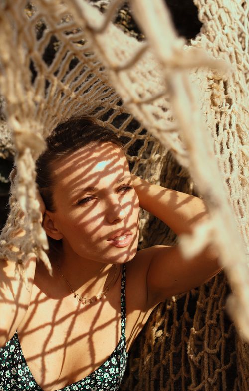 Free A woman enjoying leisure time in a sunlit hammock outdoors, casting artistic net shadows on her face. Stock Photo