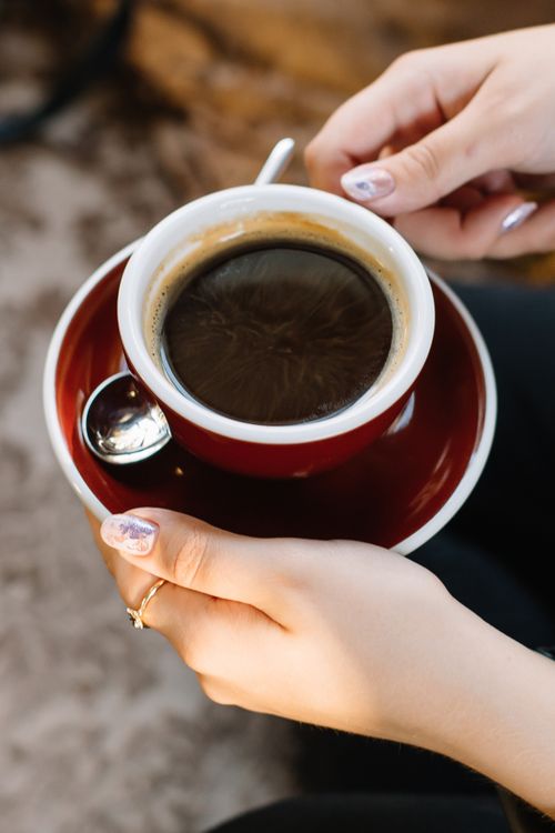 Free Woman's hands holding a hot black coffee in a red cup with saucer. Stock Photo
