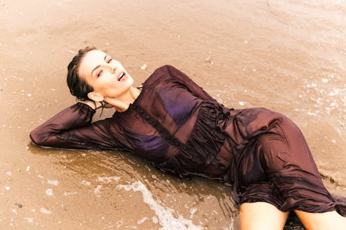 Woman in a Black Mesh Dress Posing on a Seashore and Lying in Water 